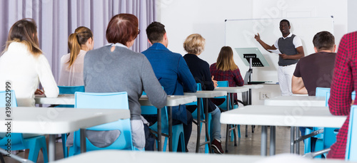 Concentrated adult students of different nationalities with teacher studying in classroom