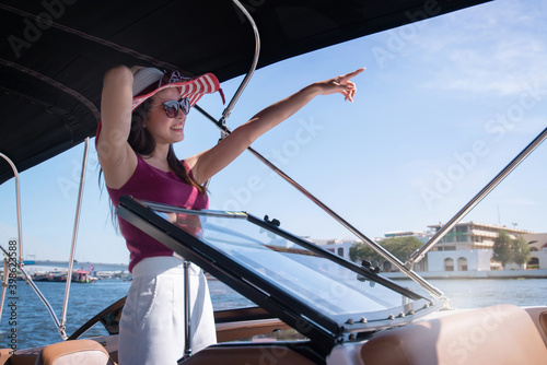 Asian beautiful woman enjoying on modern motor boat and pointing her finger, in the city of Bangkok, Thailand, Luxury summer vacation travel by modern boats on the river