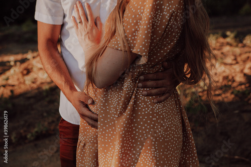 A pregnant woman and her husband and baby daddy-to-be holds hands on her stomach hugs his wife. Close-up of arms and abdomen. Pregnancy women