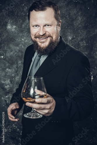 Solid smiling bearded man in suit with glass of whisky