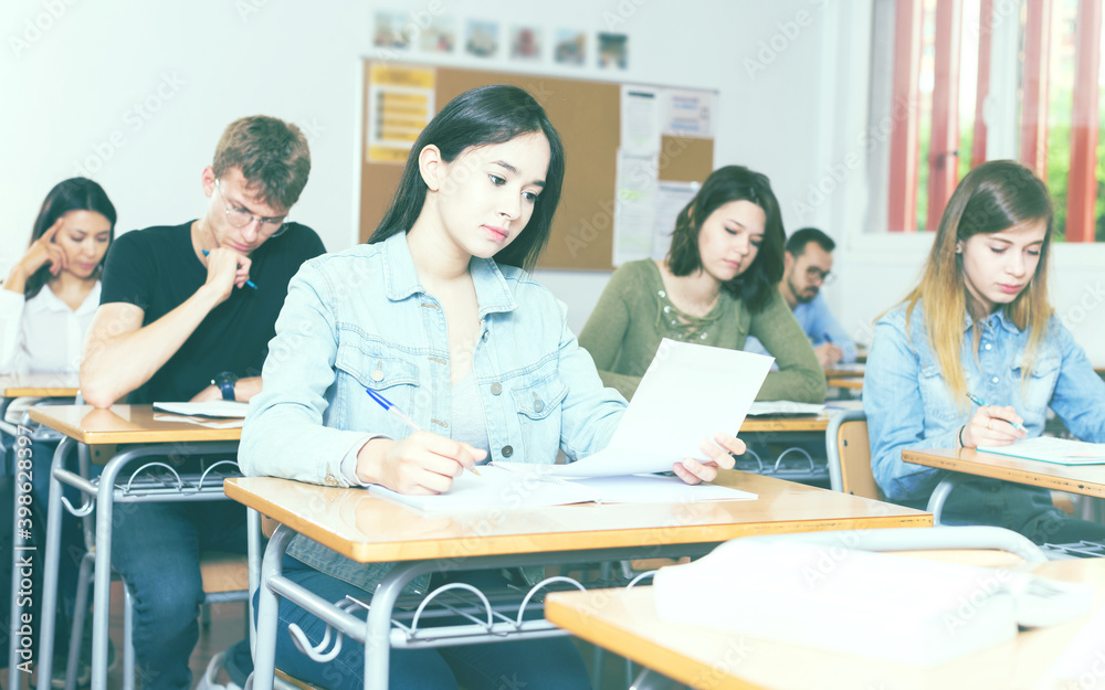 Fototapeta premium positive adult schoolgirl is sitting test and answer about task in the classroom.