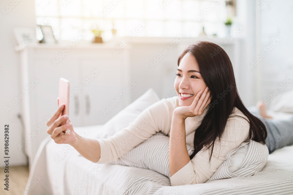 Happy young woman using video call by mobile phone and lying on the bed Happy young woman using video call by mobile phone and lying on the bed