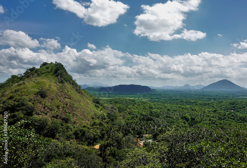 Green mountains and hills rise above the dense endless jungle. Blue sky with scenic clouds. Panorama from the top of Mount Sigiriya. Sri Lanka