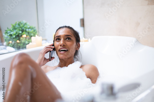 Mixed race woman lying in bath relaxing and using smartphoe photo