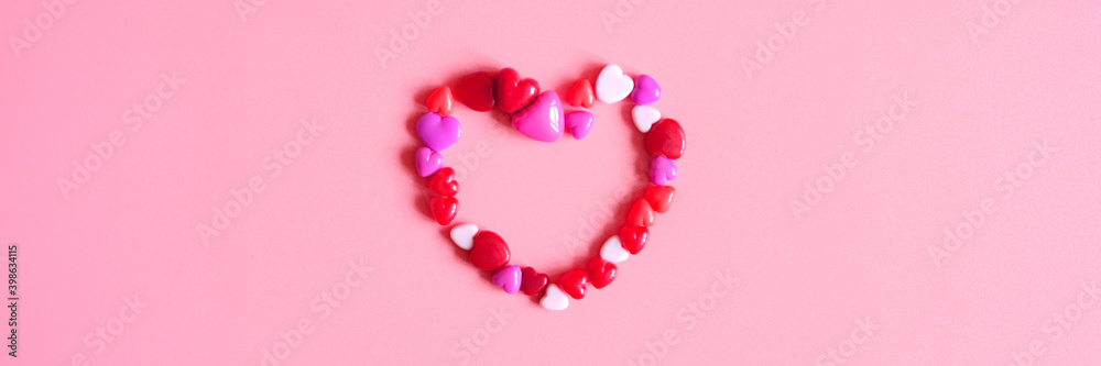 a heap of heart form glossy beads in different pink shades laid out in the shape of a heart on a pink background. banner a heap of heart form glossy beads in different pink shades laid out in the shape of a heart on a pink background. banner