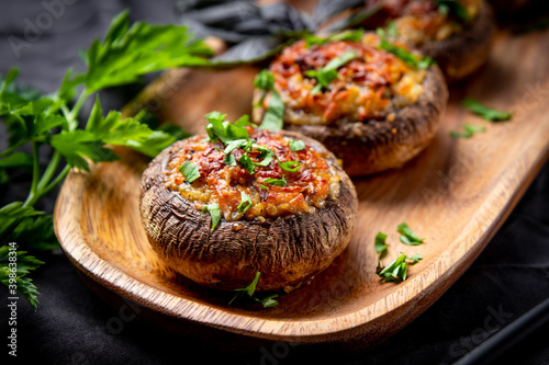 Obraz na płótnie Baked stuffed mushrooms on a wooden plate, soft focus, close up