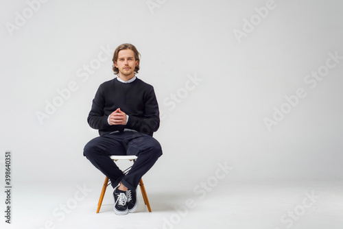 A business guy with a beard, on a white background in the studio, sits on a chair in jeans, a jacket photo