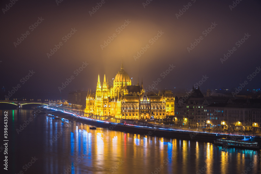 A side view of the Hungarian Parliament building along the Danube River at night with the building lit up. Budapest