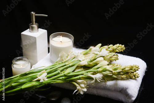 Spa composition with bunch of tuberose flowers and candle on towel, with  oil bottle pile of black stones