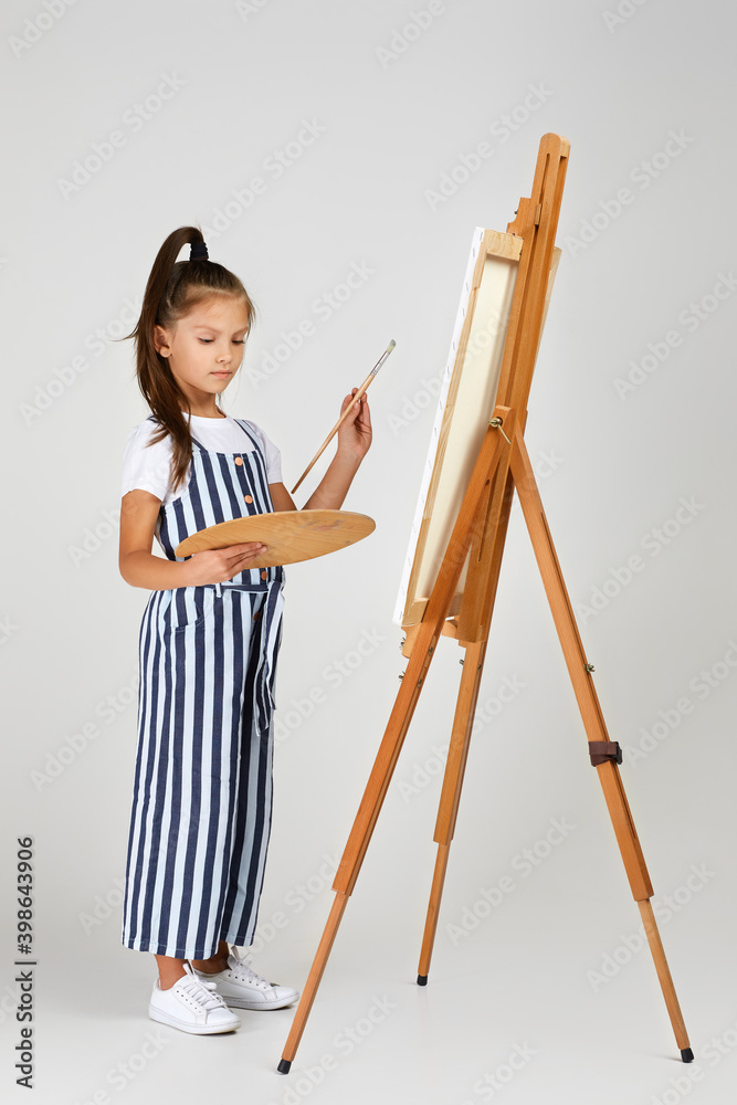 cute little girl holding a wooden art palette and brush on studio background. child painting. Full length cute little girl holding a wooden art palette and brush on studio background. child painting. Full length