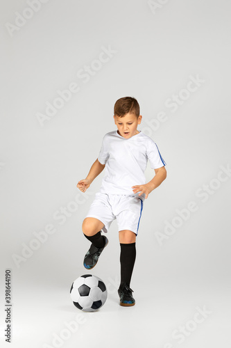 little child boy in uniform playing with soccer ball over studio background.