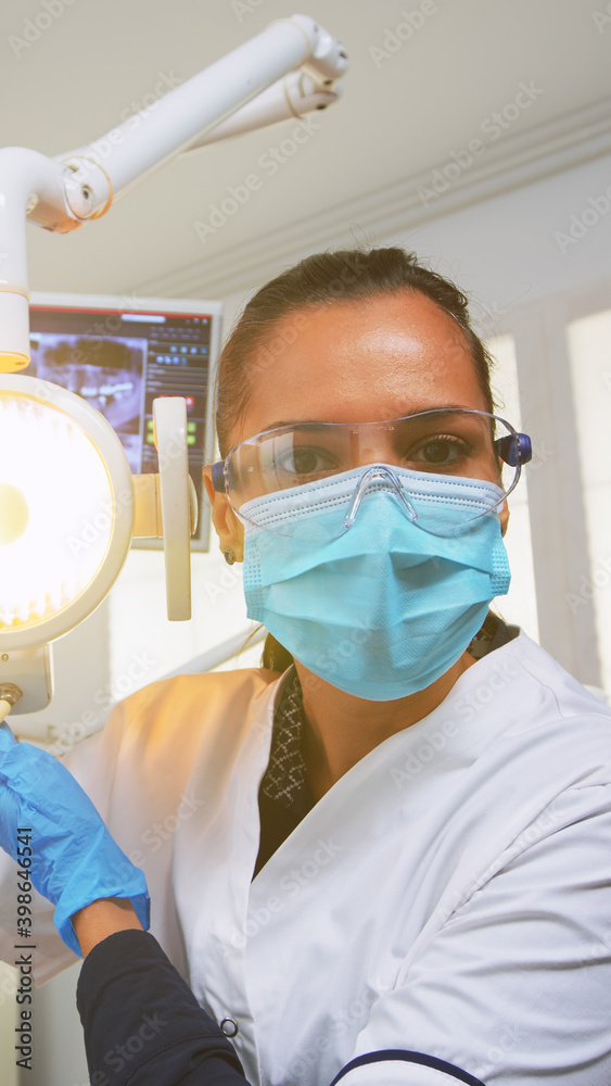 Naklejka premium Patient pov visiting dental clinic for surgery treating affected mass. Doctor and nurse working together in modern orthodontic office, lighting the lamp and examining person wearing protection mask.