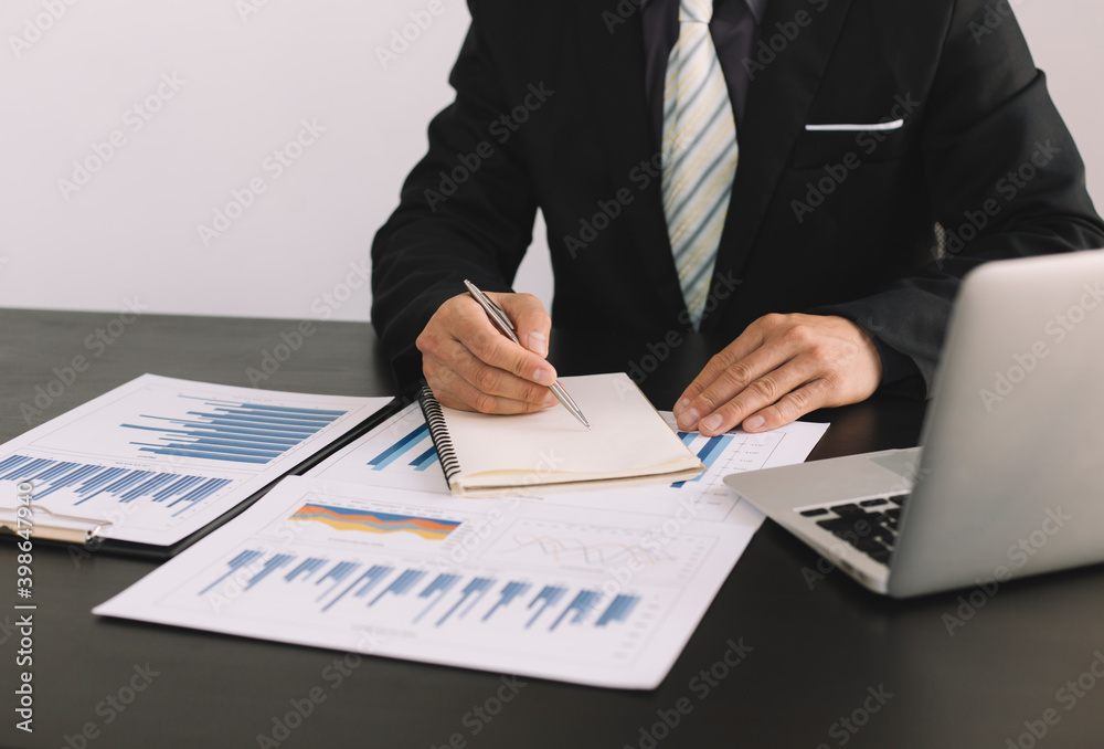 Businessmen or accountants sit, take notes or analyze data from graphs placed on their desks to assess risks and plan the future for the business. Businessmen or accountants sit, take notes or analyze data from graphs placed on their desks to assess risks and plan the future for the business.