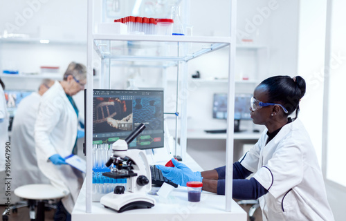 Scientist with african ethnicity conducting virus analysis with her team in modern facility. Black healthcare researcher in biochemistry laboratory wearing sterile equipment.
