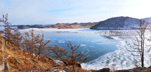 Baikal Lake in December. Panoramic view of the freezing Kurkut Bay. Thin transparent ice off the coast and open water in the bay. Rocky coast with larch trees at sunset. Beautiful winter landscape