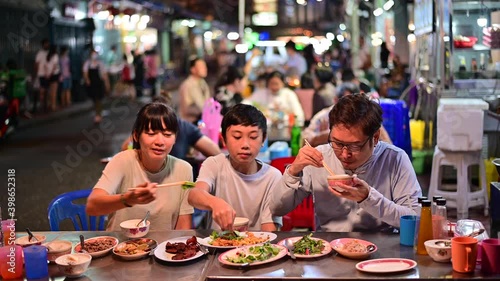 4K Asian family enjoy eating food on street food restaurant with crowd of people at Yaowarat road, Bangkok
