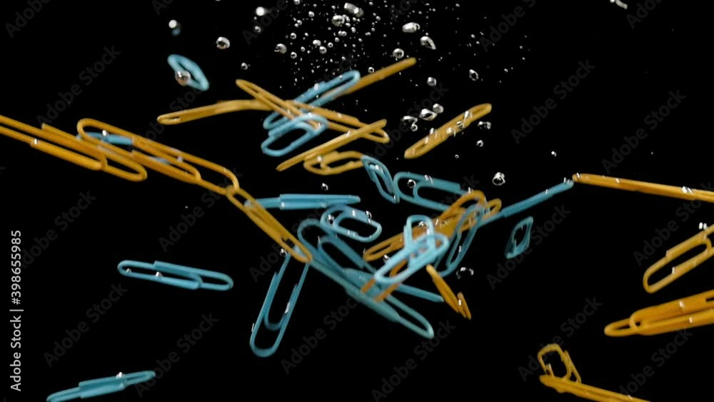 colored paper clips drown in water, shooting in an aquarium on a black background, immersing objects at speed into liquid