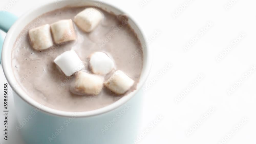 A Cup of cocoa with marshmallows falling into it.
