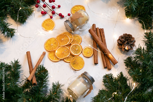 Christmas still life. Dried orange slices, cinnamon sticks, candles in a glass jar and a garland that creates a new year's mood! Spruce twigs and cones