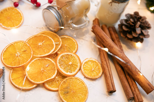 Christmas still life. Dried orange slices, cinnamon sticks, candles in a glass jar and a garland that creates a new year's mood Christmas cone