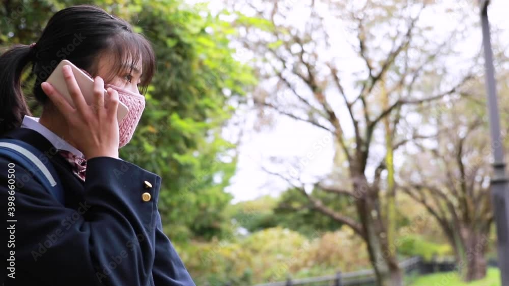 スマートフォンで話すマスクをつけた日本人女子学生 スマートフォンで話すマスクをつけた日本人女子学生