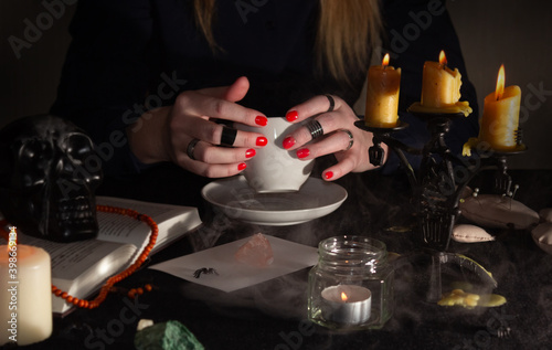 Fortune-telling on coffee grounds. A fortune teller's hands, a Cup of coffee, candles, and skulls on a black table. The concept of wizards, witchcraft and magic.