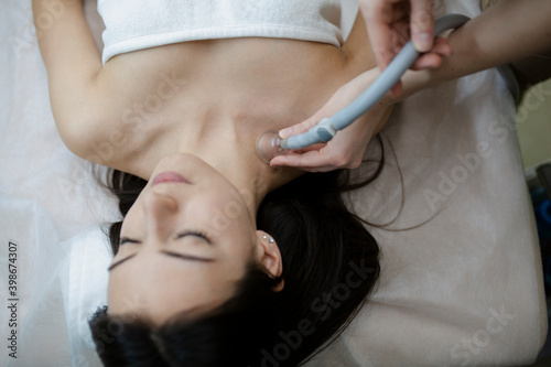 Young beautiful woman in spa. Cosmetologist with roller doing vacuum roller massage for her female client young woman in modern spa medical center. photo