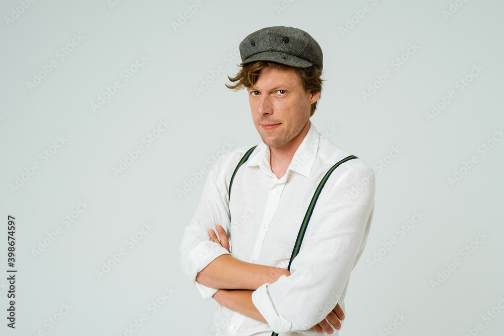 Hipster man posing with hands folded dressed in white shirt and grey wool cap isolated on white background. Copy space at left side. Hipster man posing with hands folded dressed in white shirt and grey wool cap isolated on white background. Copy space at left side.