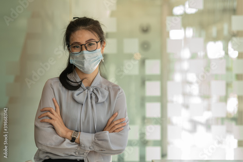 Business Asian women stand and wear masks and cross arms in the office.