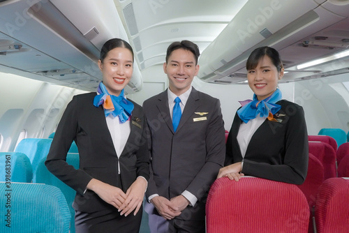 Obraz na plátně Portrait of three man and woman in blue suit flight attendant/air hostess in economy class cabin smiling to welcome passenger at airplane