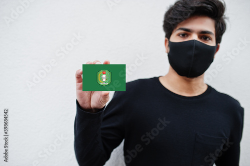 Indonesian man wear all black with face mask hold West Kalimantan flag in hand isolated on white background. Provinces of Indonesia coronavirus concept. photo