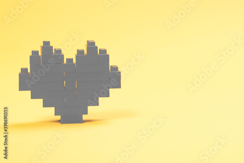 Gray heart made of plastic constructor blocks on yellow background.