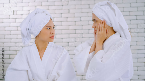 Two Asian girls in white bathrobes with towels on heads talking in living room.