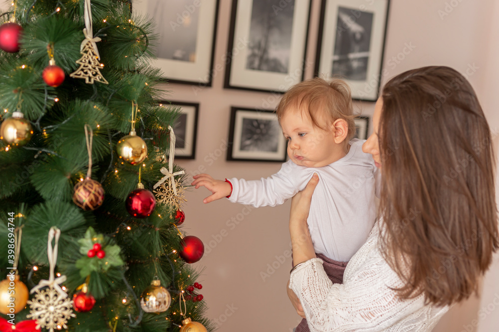 Mother holding her baby boy and decorating Christmas tree Mother holding her baby boy and decorating Christmas tree