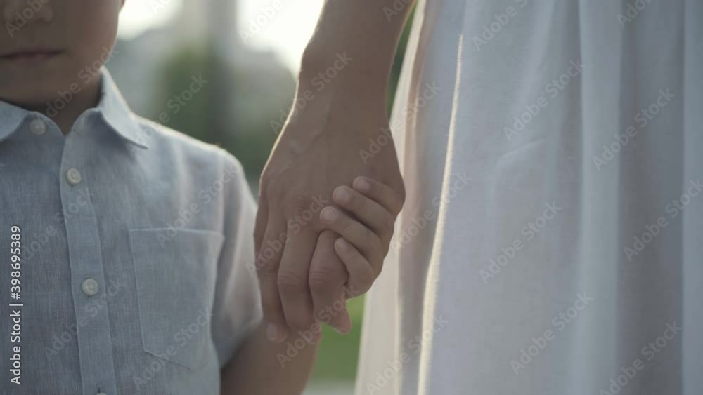 Close-up of unrecognizable little boy taking mother's hand in sunlight. Cute charming Middle Eastern child enjoying leisure outdoors with confident woman. Family lifestyle concept. Close-up of unrecognizable little boy taking mother's hand in sunlight. Cute charming Middle Eastern child enjoying leisure outdoors with confident woman. Family lifestyle concept.