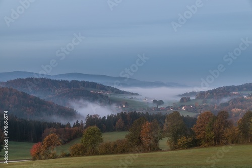 Landschaft im Sonnenaufgang im Nebel am Morgen mit Wiese Feld Acker Wald Baum Berge im Hintergrund bei Grafenau im Bayerischer Wald im Herbst, Deutschland © stgrafix