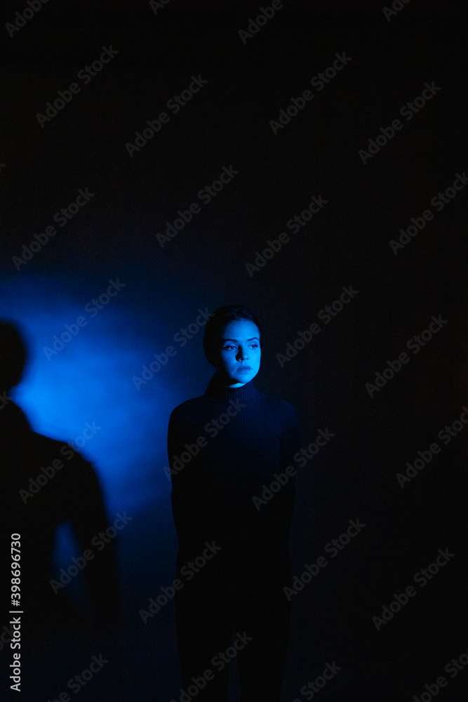 Studio portrait of a young girl in the darkness with blue light