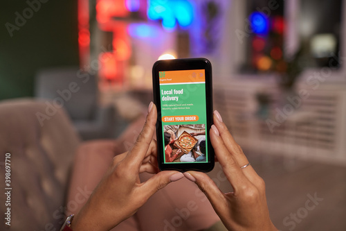 Close-up of woman holding mobile phone and ordering food online while lying on the sofa