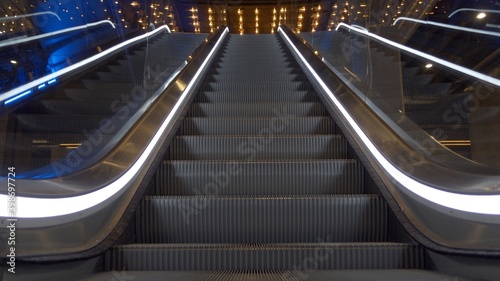 Close up of upward moving stairs with white lights on sides in business and shopping centre with no people around  © Sia