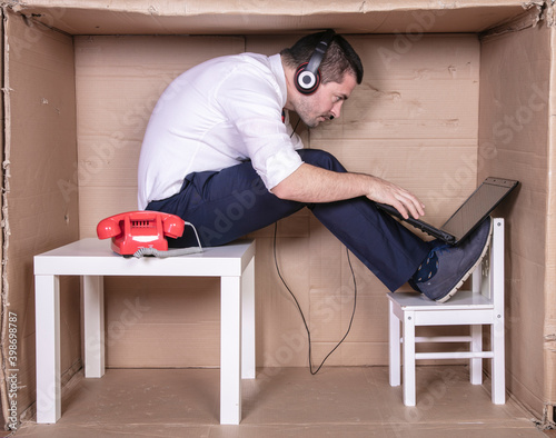 businessman in a cramped cardboard office trying to focus on his work photo