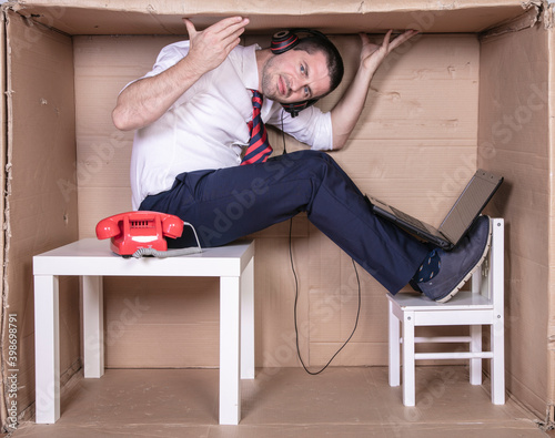 Fotografi businessman in a cramped cardboard office trying to focus on his work