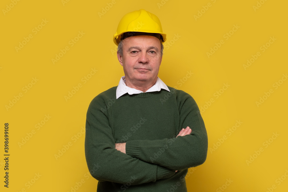 Senior caucasian foreman with hard hat. Studio shot on yellow wall.