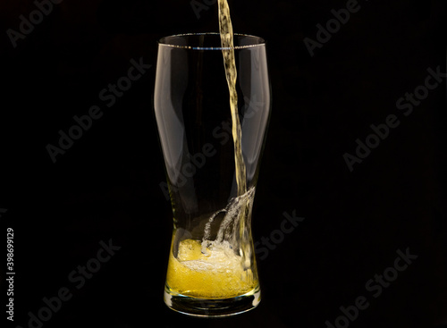 Pouring lager beer into a glass, isolated on black background, space for copy