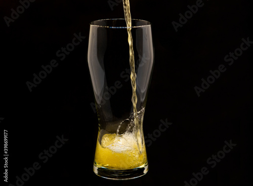 Pouring lager beer into a glass, isolated on black background, space for copy