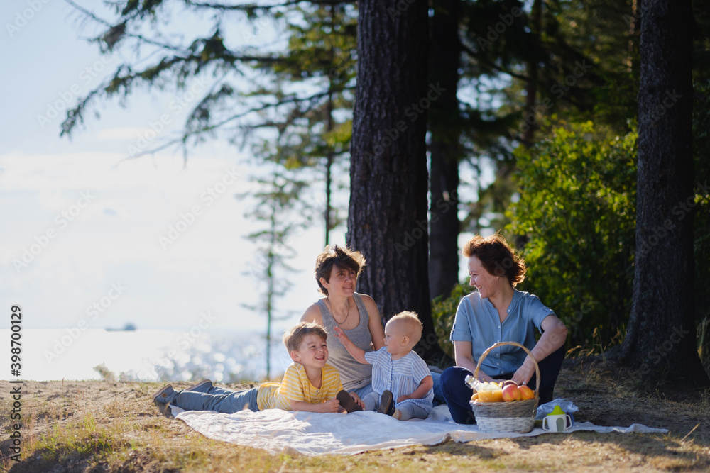 Homosexual lesbian family with two children, a son and a daughter. Two moms and kids at an outdoor picnic. Forest and sea.