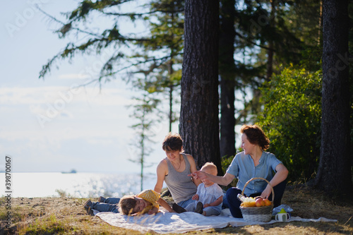 Homosexual lesbian family with two children, a son and a daughter. Two moms and kids at an outdoor picnic. Forest and sea. © spaskov