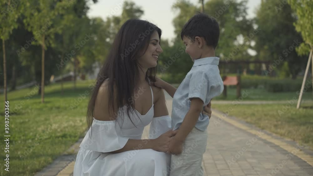 Positive young mother sitting on hunkers and talking to cute little son. Middle Eastern woman enjoying summer weekend with charming boy. Happiness and motherhood concept. Positive young mother sitting on hunkers and talking to cute little son. Middle Eastern woman enjoying summer weekend with charming boy. Happiness and motherhood concept.