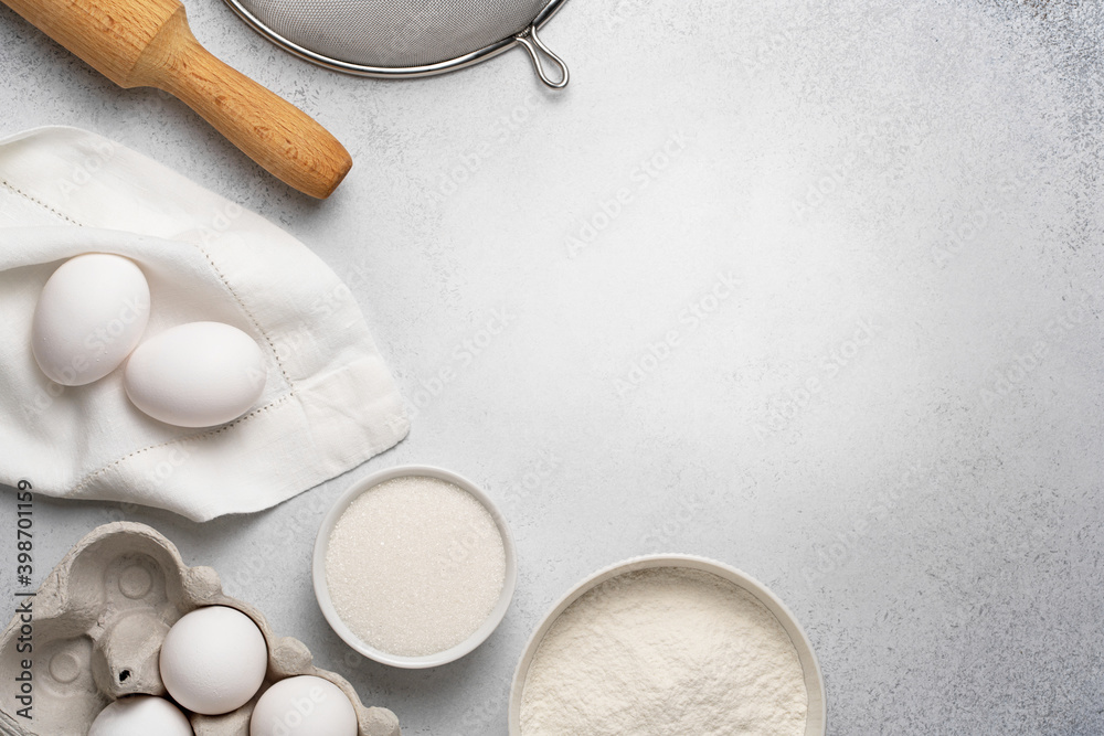 Wheat flour, sugar, sieve, rolling pin and white eggs on napkin on grey background. Flat lay with baking ingredients for dough. Top view, copy space. Wheat flour, sugar, sieve, rolling pin and white eggs on napkin on grey background. Flat lay with baking ingredients for dough. Top view, copy space.