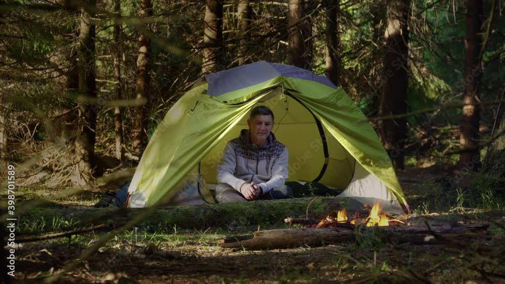 A man in a tent near a fire in the woods. Camping in a beautiful forest. Travel concept A man in a tent near a fire in the woods. Camping in a beautiful forest. Travel concept
