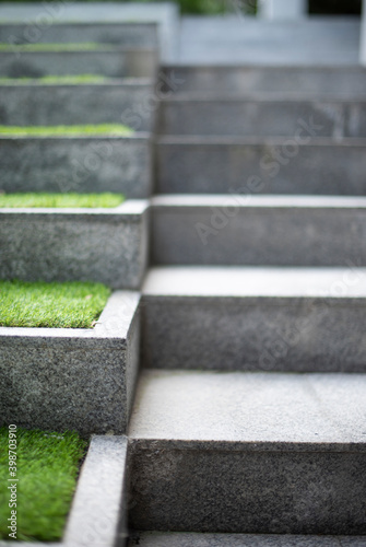 Neat and tidy grey stair steps made of stone and granite tiles with a curb, side by side with green steps in a modern hotel leading to a lobby area, close up.